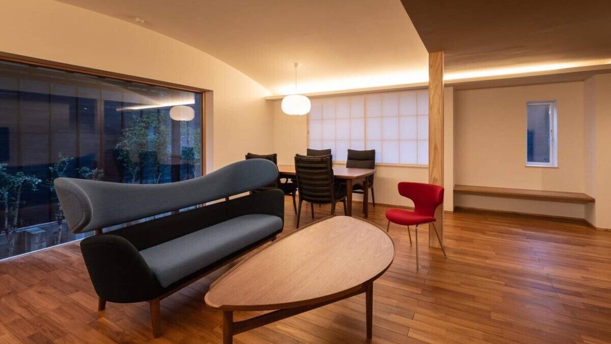 Ein modernes Wohnzimmer mit einer Couch, einem Esstisch, Stühlen und einem großen Fenster.