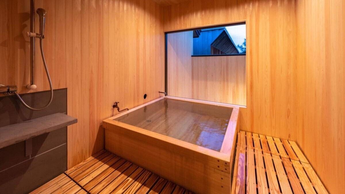 A wooden sauna with a glass-enclosed tub, a wooden bench, and a window with a view.