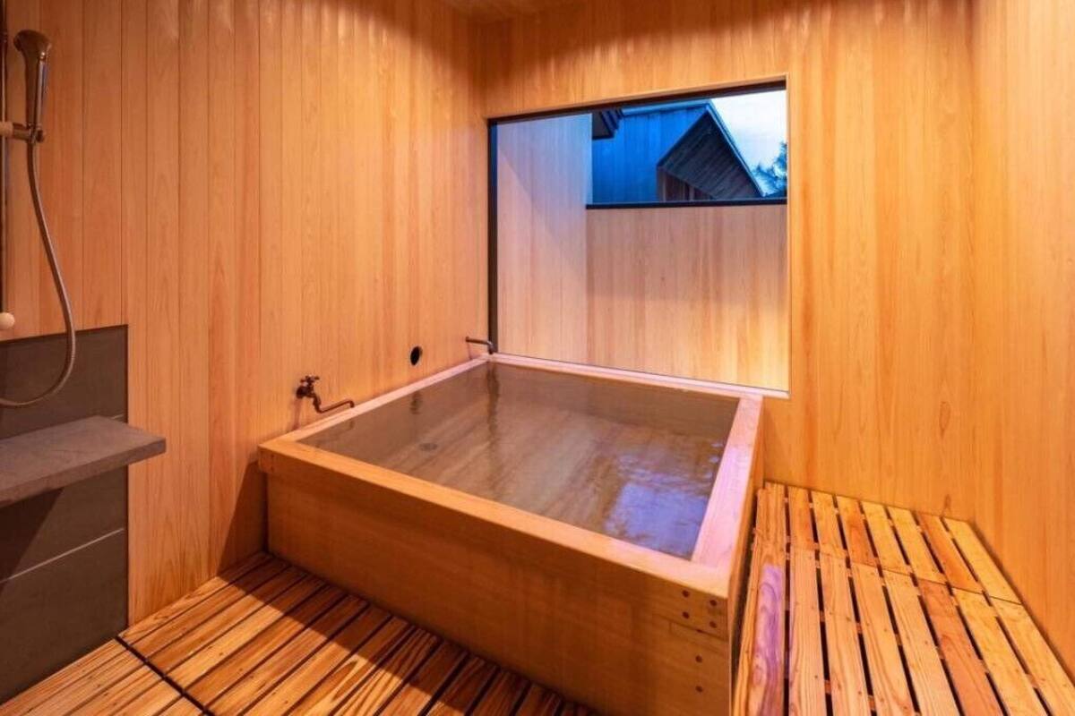 Un sauna en bois doté d’une baignoire entourée de parois en verre, d’un banc en bois et d’une fenêtre offrant une vue panoramique.