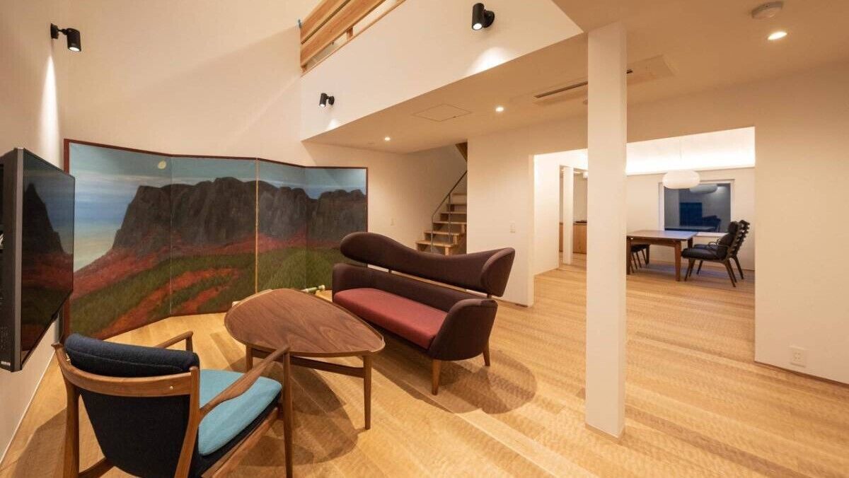 A modern interior with a wooden floor, a sofa, a dining table, and a staircase.