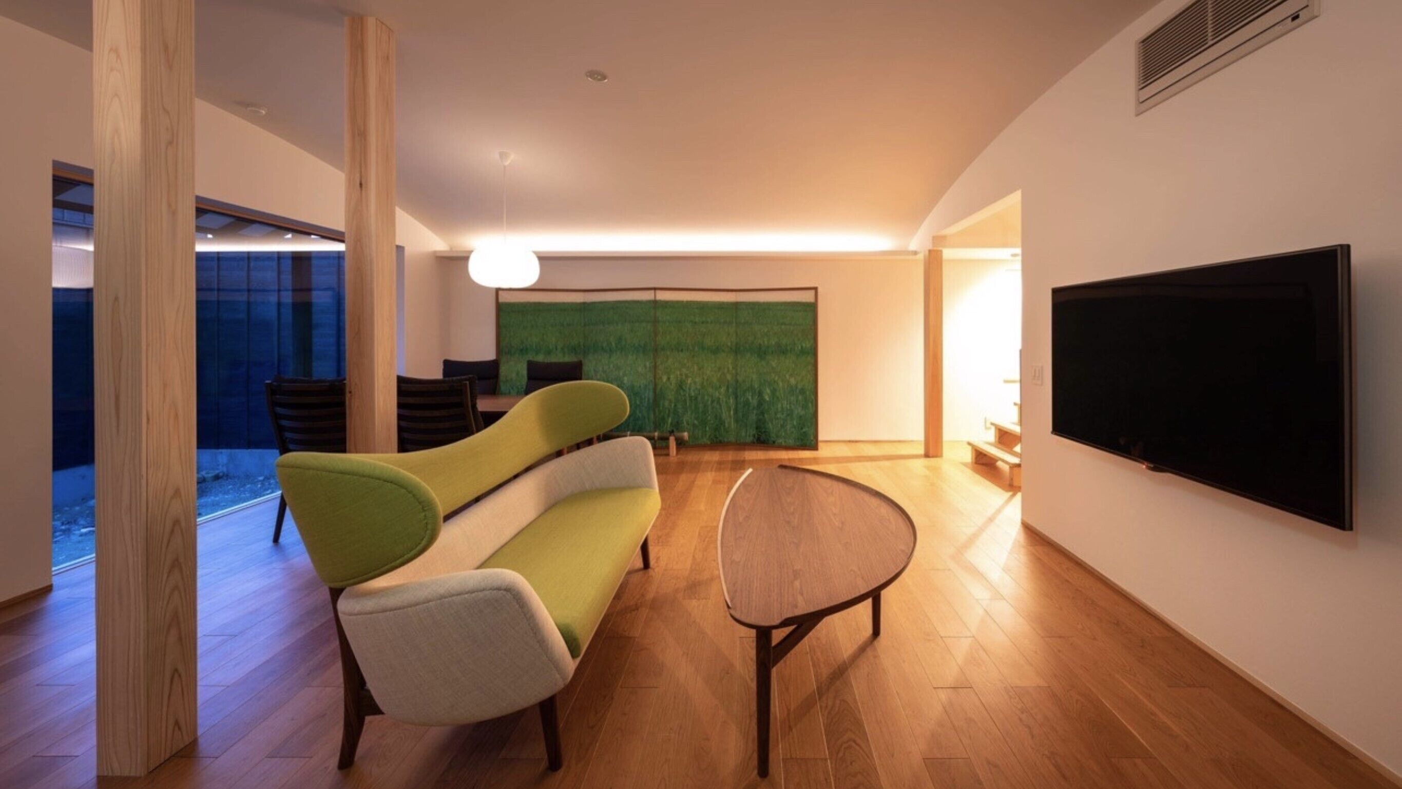 A modern living room with a large flat-screen TV, a green sofa, a round table, and a large abstract painting on the wall.