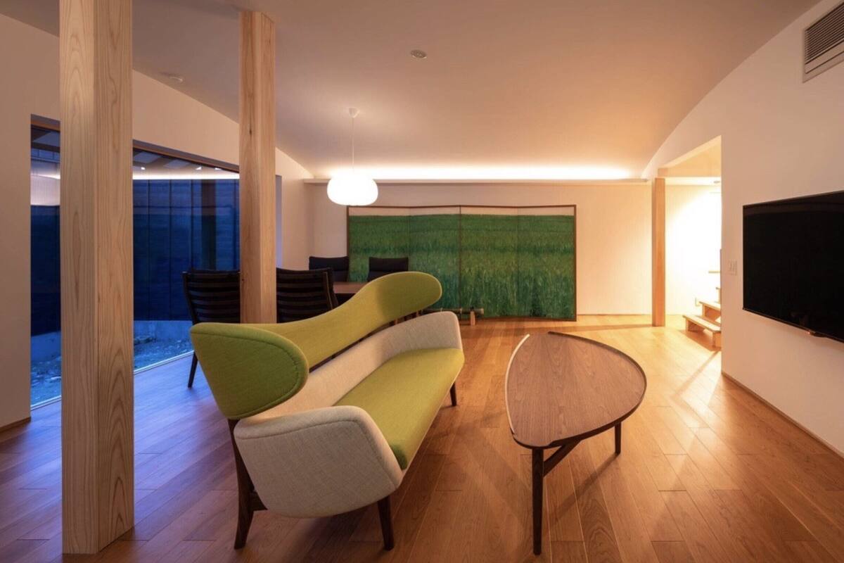 Un salon moderne doté d’un grand téléviseur à écran plat, d’un canapé vert, d’une table ronde et d’un grand tableau abstrait accroché au mur.