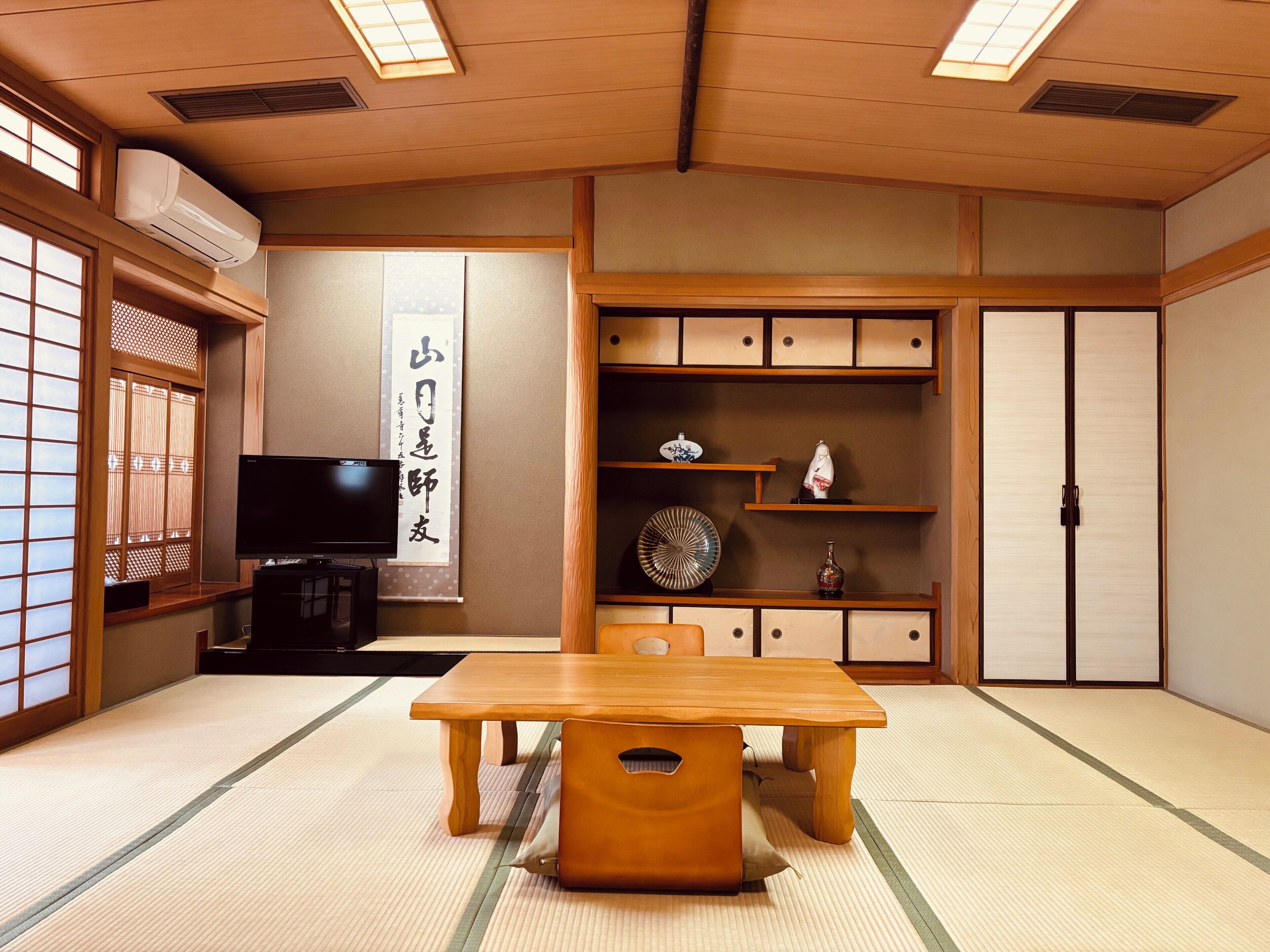 A traditional Japanese room with tatami flooring, a television, a wooden table, and sliding doors.