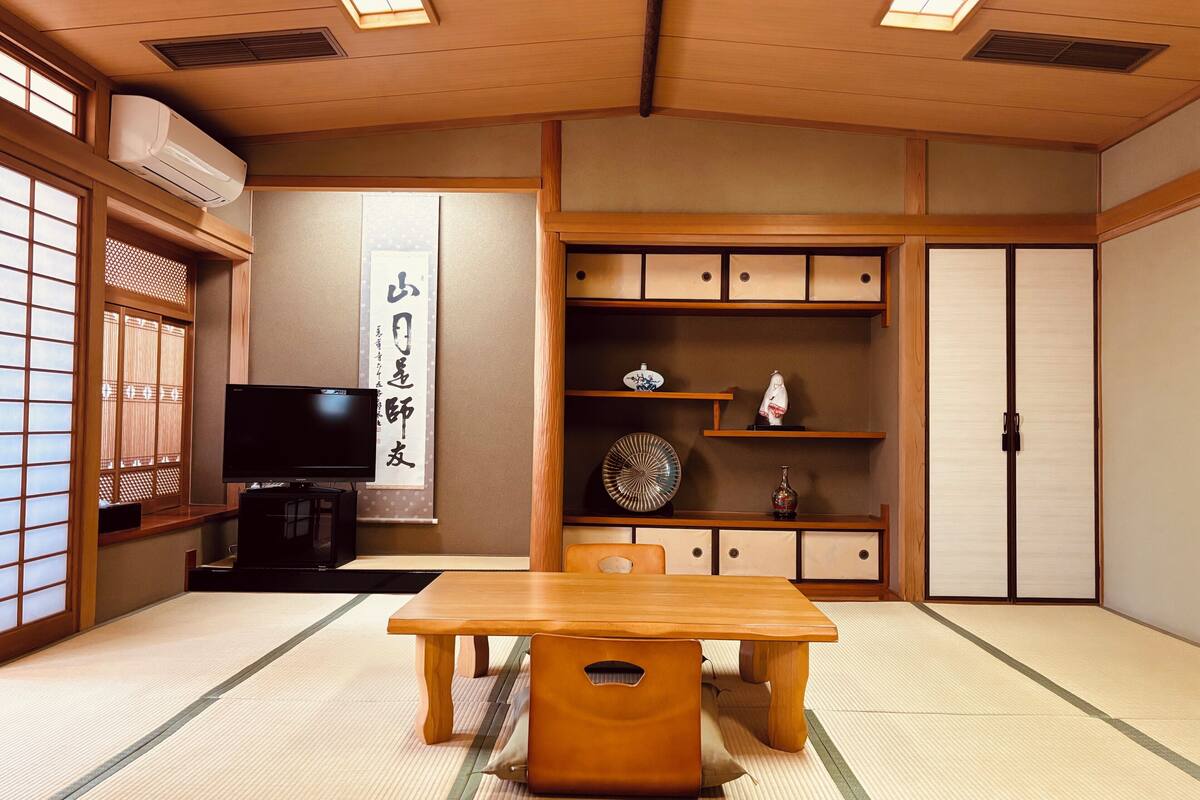 A traditional Japanese room with tatami flooring, a television, a wooden table, and sliding doors.