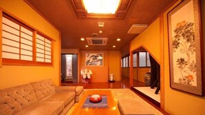 A traditional Japanese room with tatami flooring, a low wooden table, a sofa, and a large framed artwork on the wall. - Beppu Onsen Shinhorii (Beppu)