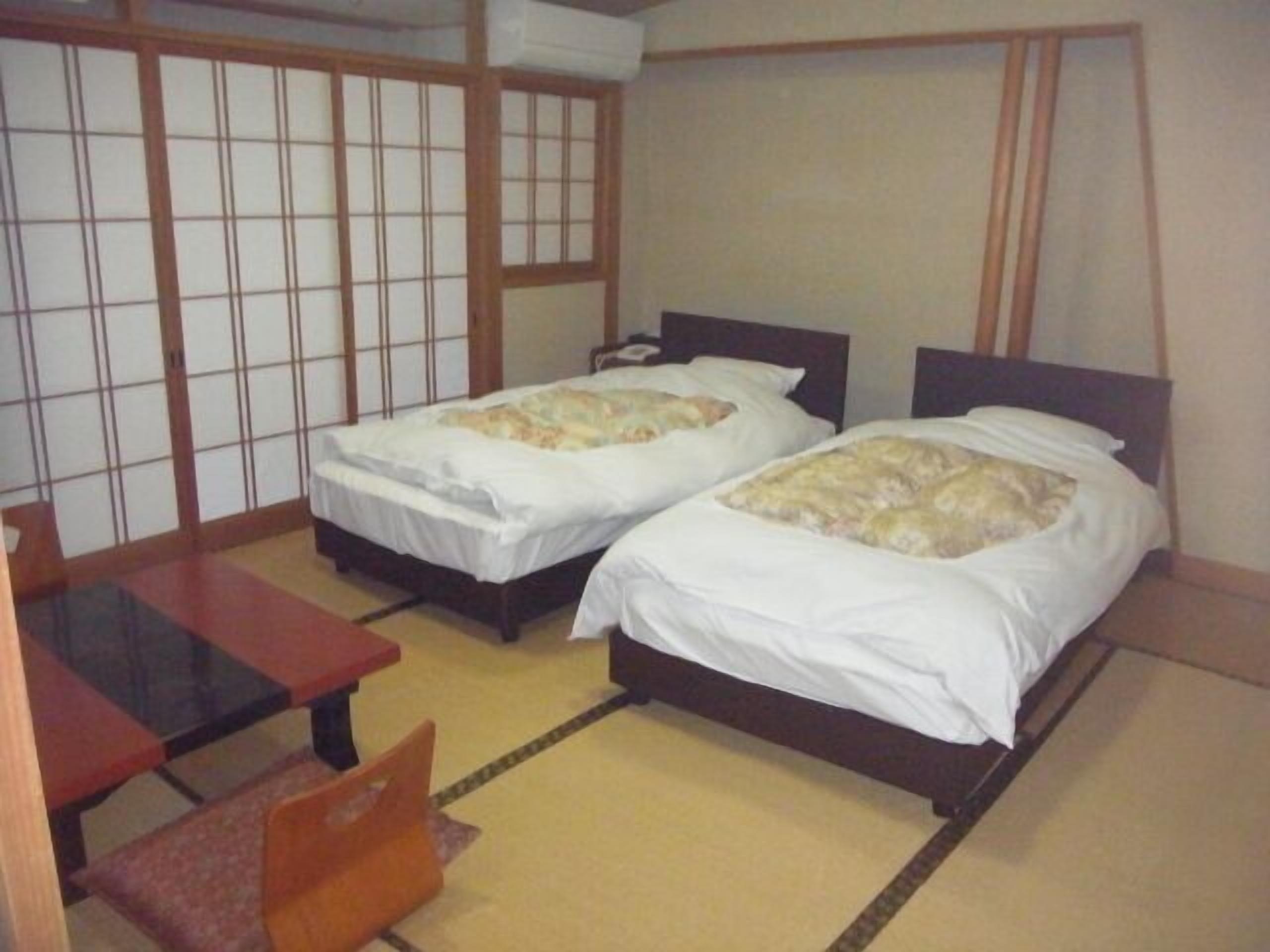 Ein Zimmer mit zwei Betten, einem kleinen Tisch und einer traditionellen Schiebetür.