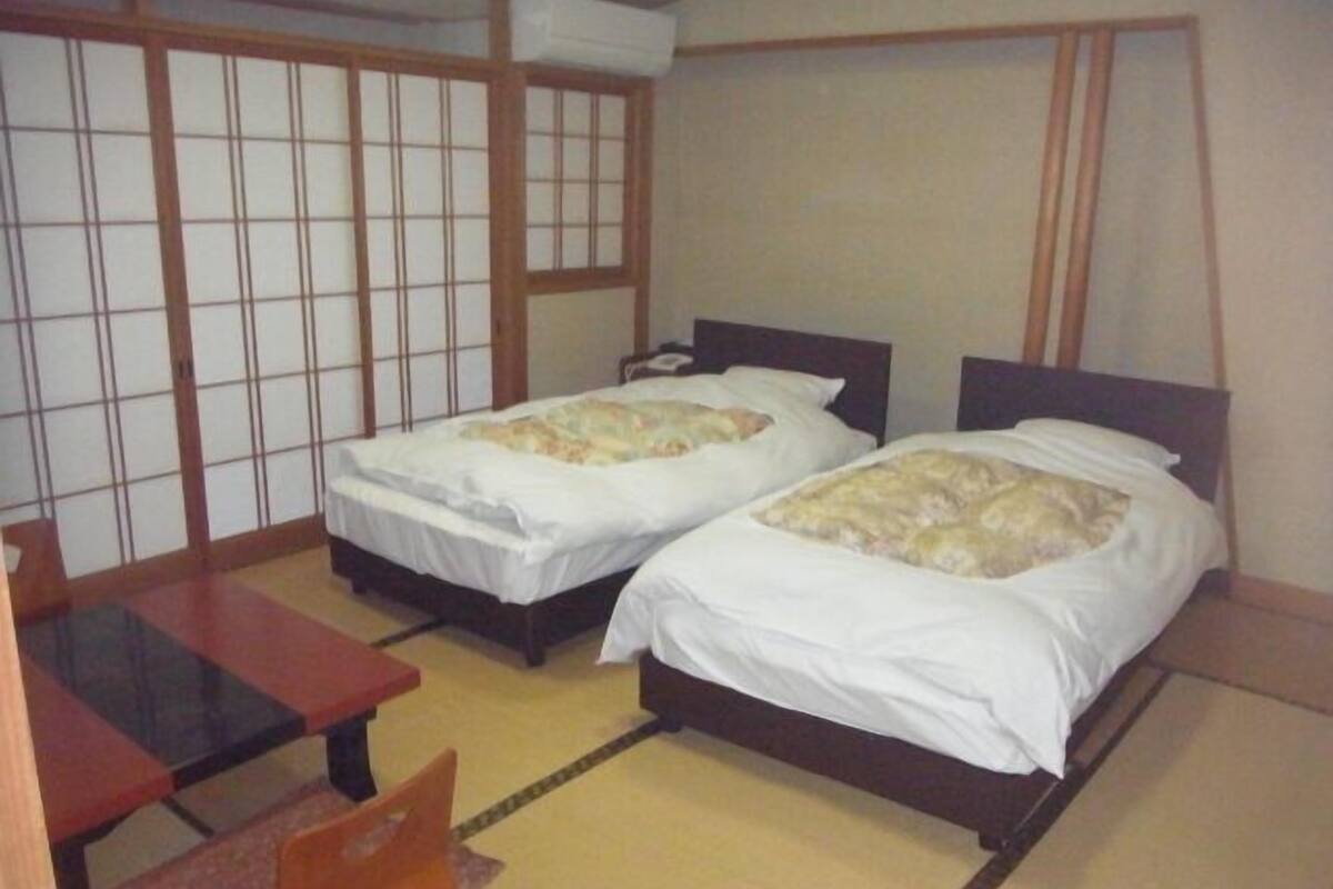 A room with two beds, a small table, and a traditional sliding door.