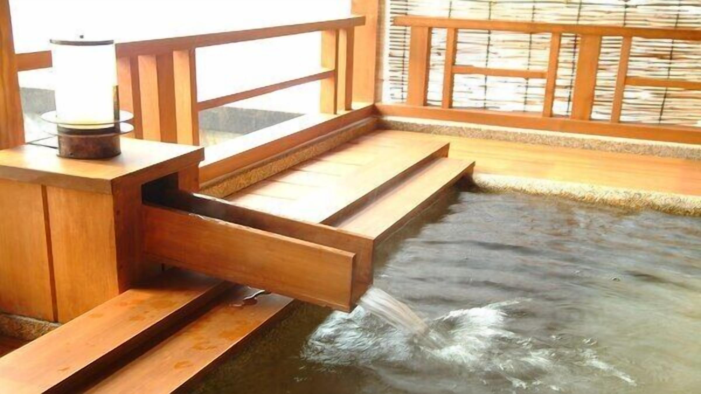 A wooden bathhouse with a hot spring, wooden steps leading into the water, and a wooden railing.