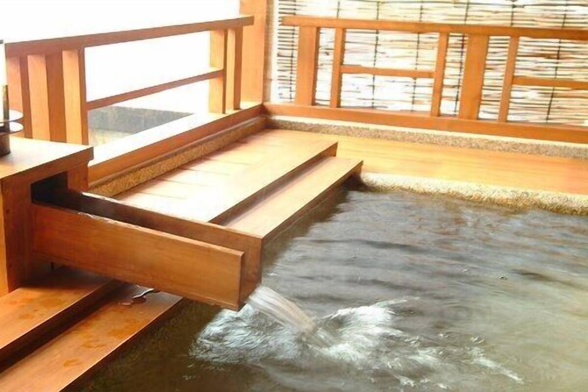 A wooden bathhouse with a hot spring, wooden steps leading into the water, and a wooden railing.