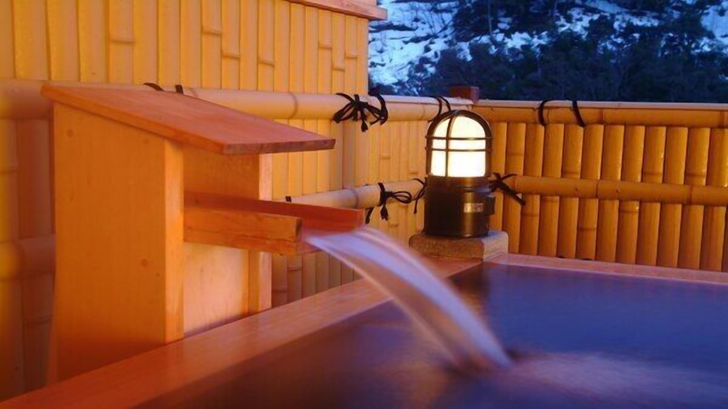 A wooden hot spring bath with a bamboo fence and a lantern.