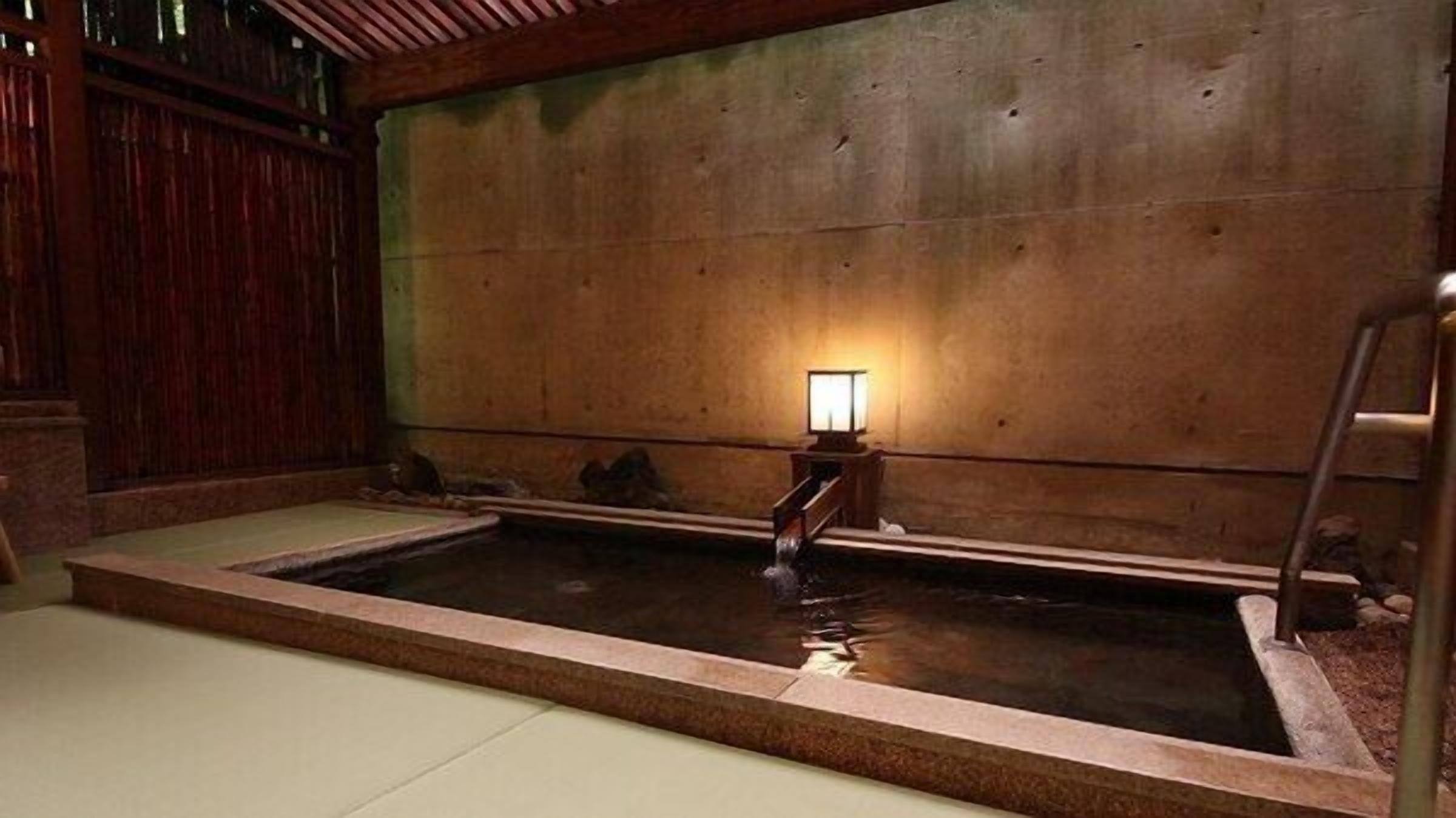 A traditional Japanese onsen with a wooden interior, a stone bath, and a small wooden bench.