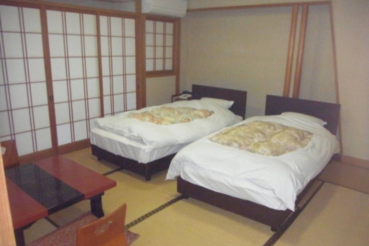 A room with two beds, a small table, and a futon.