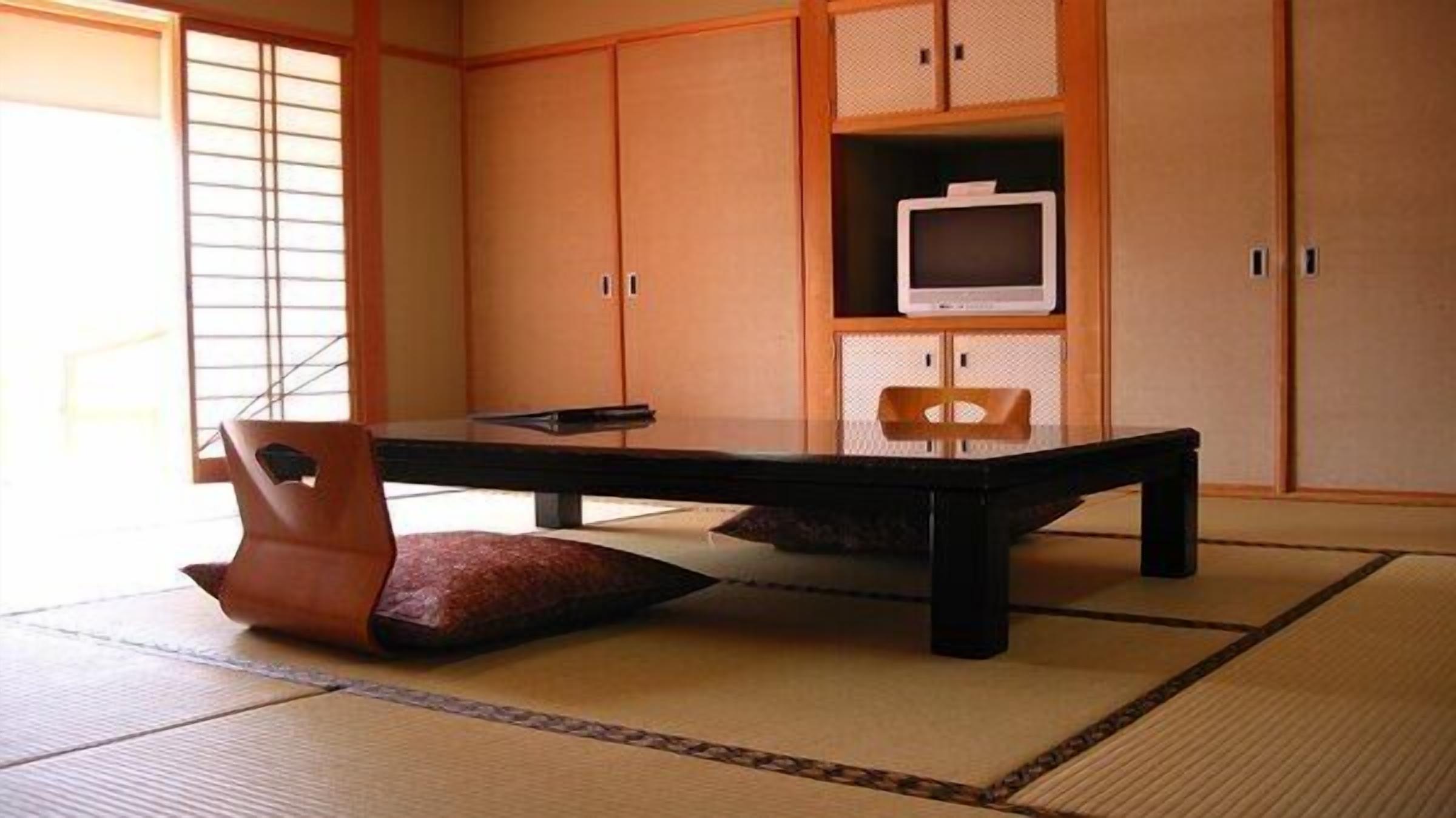 Ein traditioneller japanischer Raum mit Tatami-Bodenbelag, einem niedrigen Tisch, einem gepolsterten Sessel und Schiebetüren.