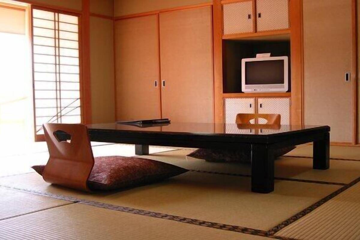 A traditional Japanese room with tatami flooring, a low table, a cushioned chair, and sliding doors.