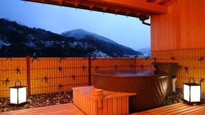 Terraza de madera con un jacuzzi, faroles y vistas a una montaña nevada.