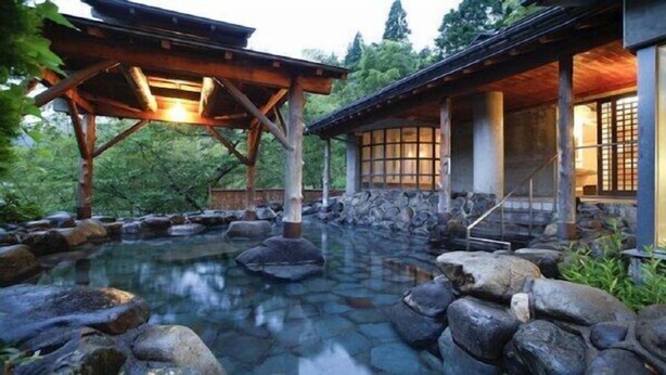 Un edificio de estilo japonés tradicional con un estanque de piedra, estructuras de madera y un jardín tranquilo.