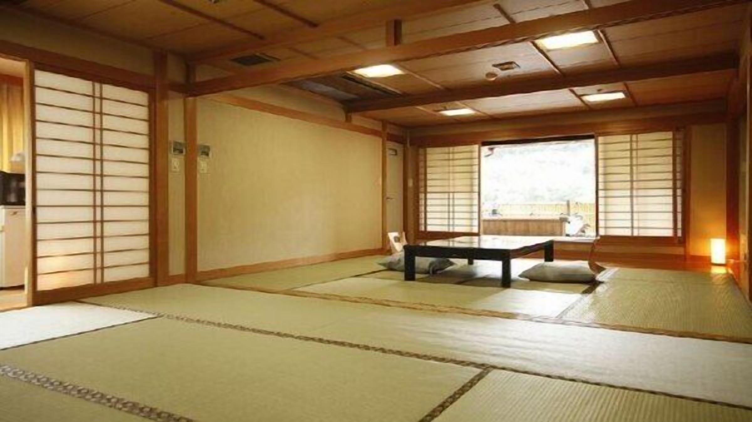 Ein traditioneller japanischer Raum mit Tatami-Böden, Schiebetüren und einem niedrigen Tisch mit Kissen.