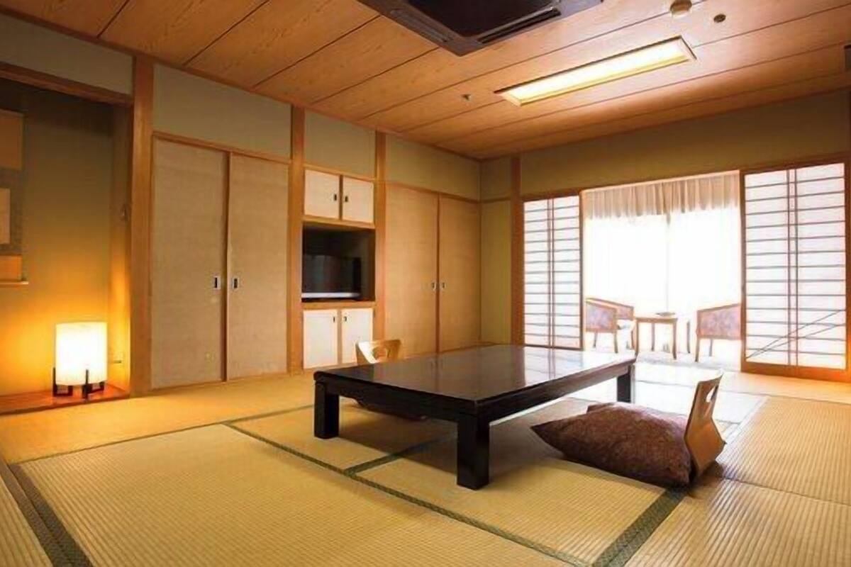 A traditional Japanese room with tatami flooring, a low table, sliding doors, and a view through a shoji screen.