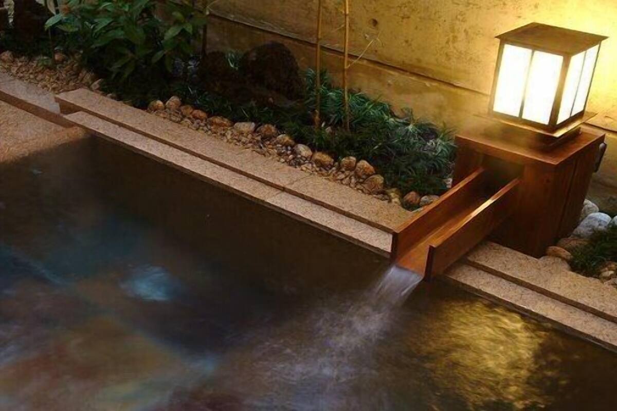 A small indoor pool with a wooden edge and a stone border, a wooden bench, and a wall-mounted lamp.