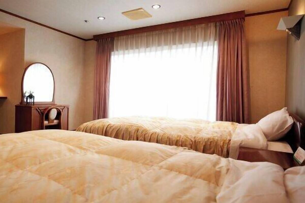 A hotel room with two beds, a dresser, a mirror, and a window with curtains.