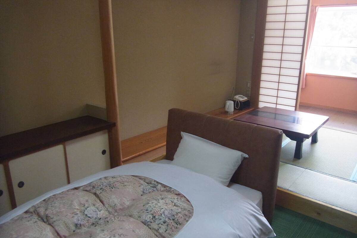 A room with a bed, a small table, and a window with a view.