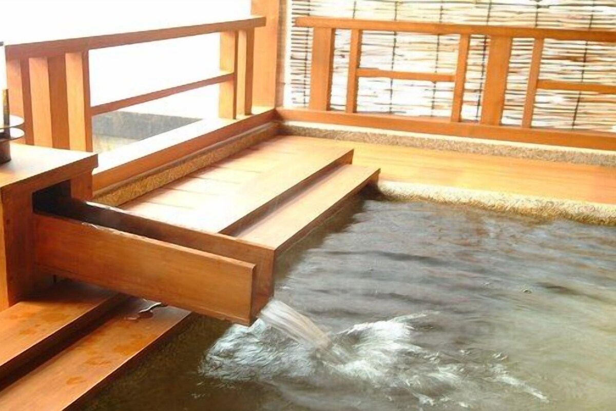 A wooden bathhouse with a hot spring, wooden steps leading into the water, and a wooden railing.
