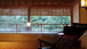 Una habitación con techo de madera, un ventanal con vistas a árboles, un banco y una silla.