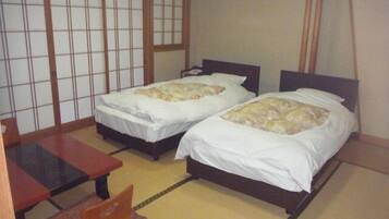 A room with two beds, a small table, and a traditional sliding door.