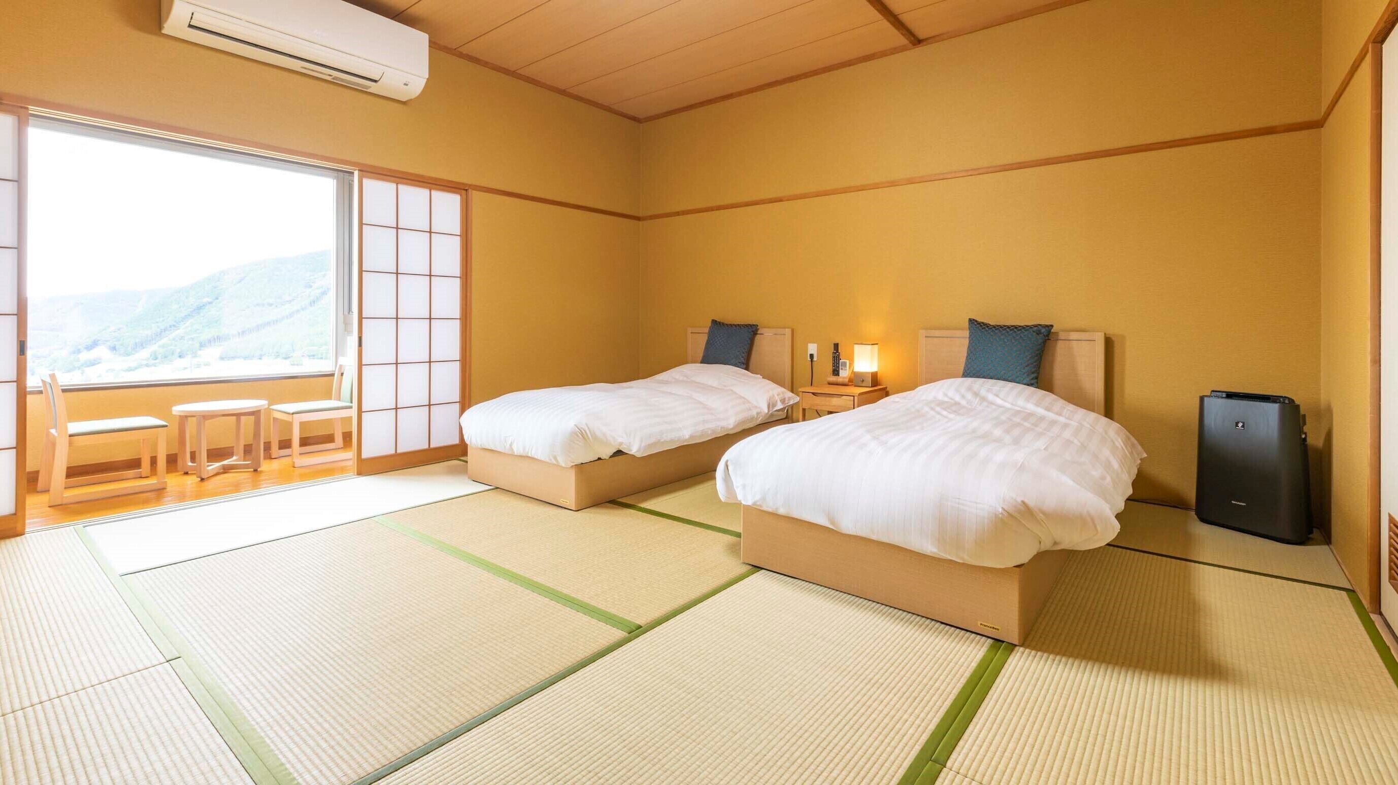 Quarto de hotel com duas camas, porta de correr para uma varanda, mesa de cabeceira com abajur e um alto-falante.