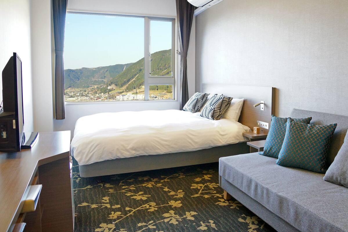 Une chambre d’hôtel équipée d’un lit, d’un canapé, d’un bureau et offrant une vue sur un paysage montagneux.