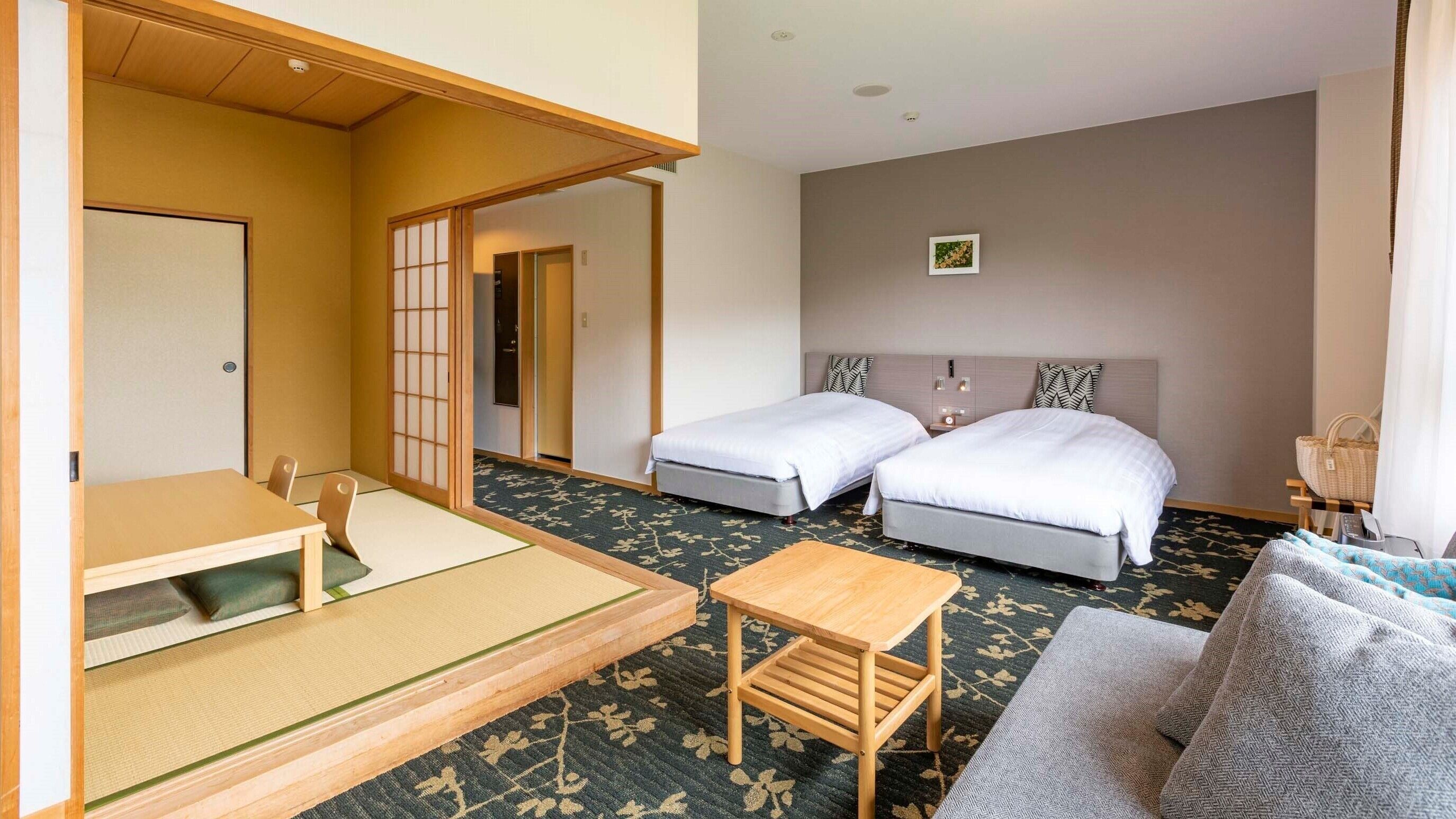 Quarto de hotel com duas camas, uma mesa pequena, um sofá, piso de tatame e um biombro shoji.