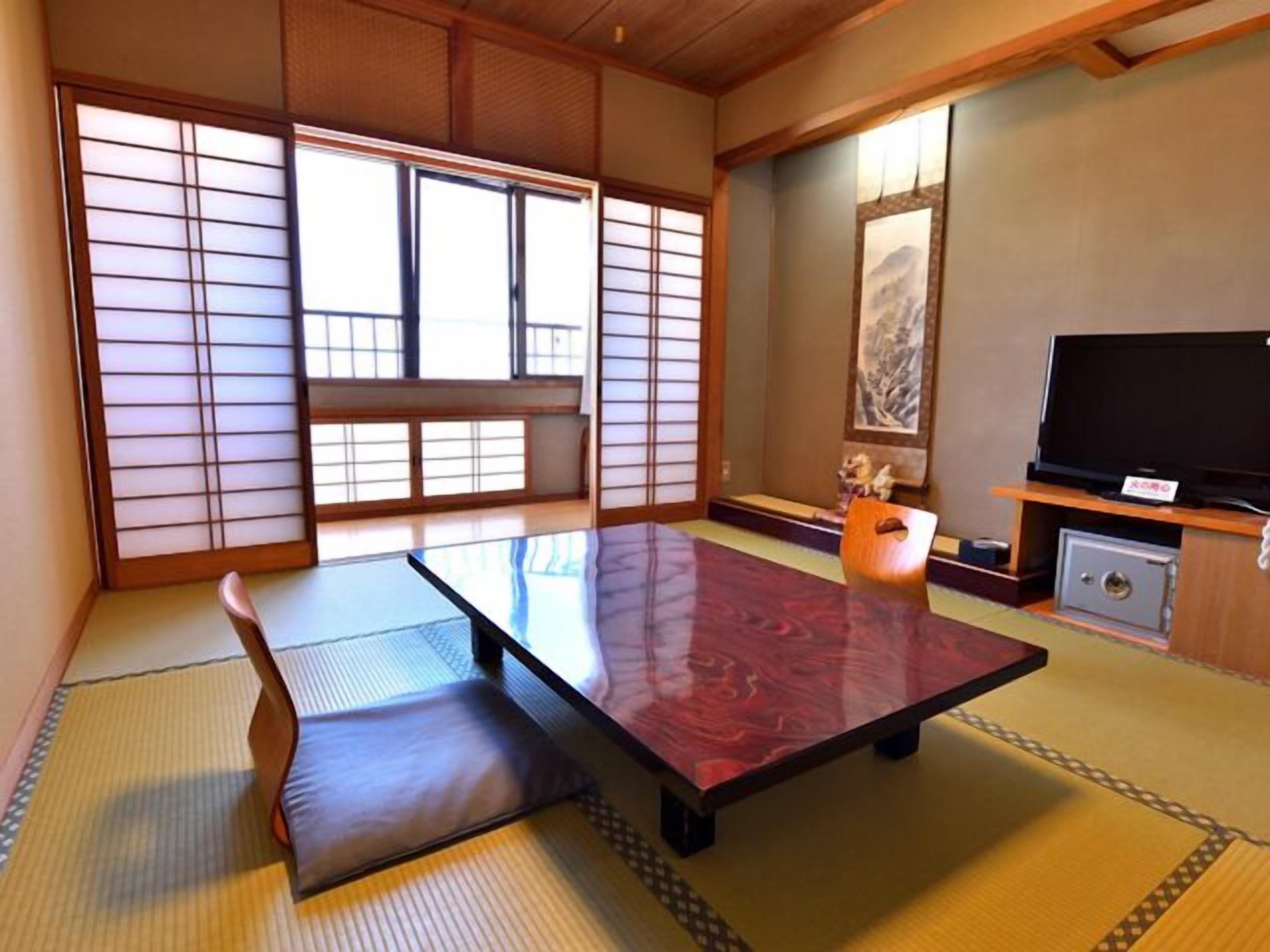 A traditional Japanese room with tatami flooring, a low table, a sofa, sliding doors, and a television.