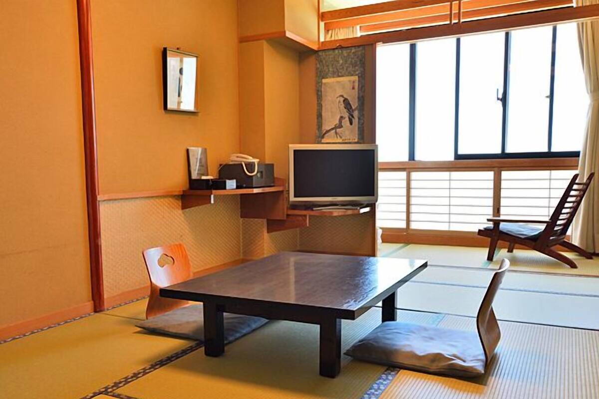 A tatami mat room with a low table, a chair, a television, and a window with a view.