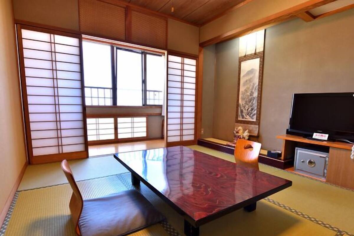 A traditional Japanese room with tatami flooring, a low table, a television, and a painting on the wall.