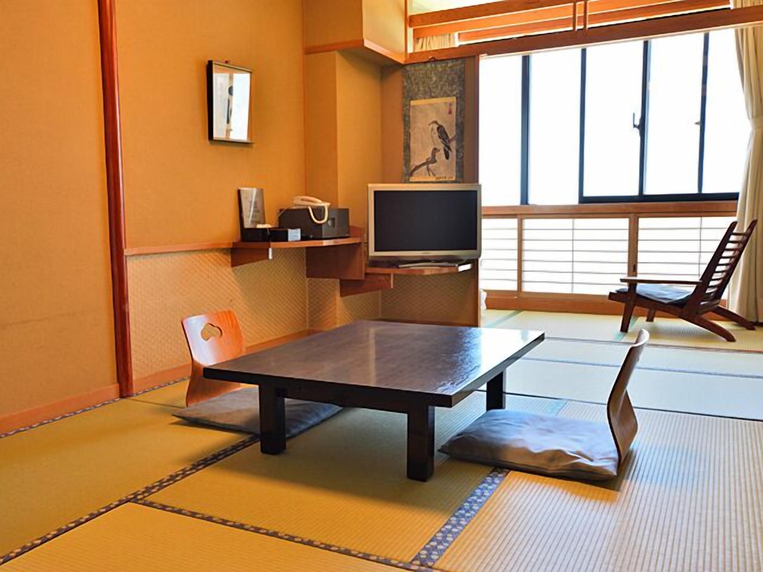 A tatami mat room with a low table, a chair, a TV, and a window with a view.