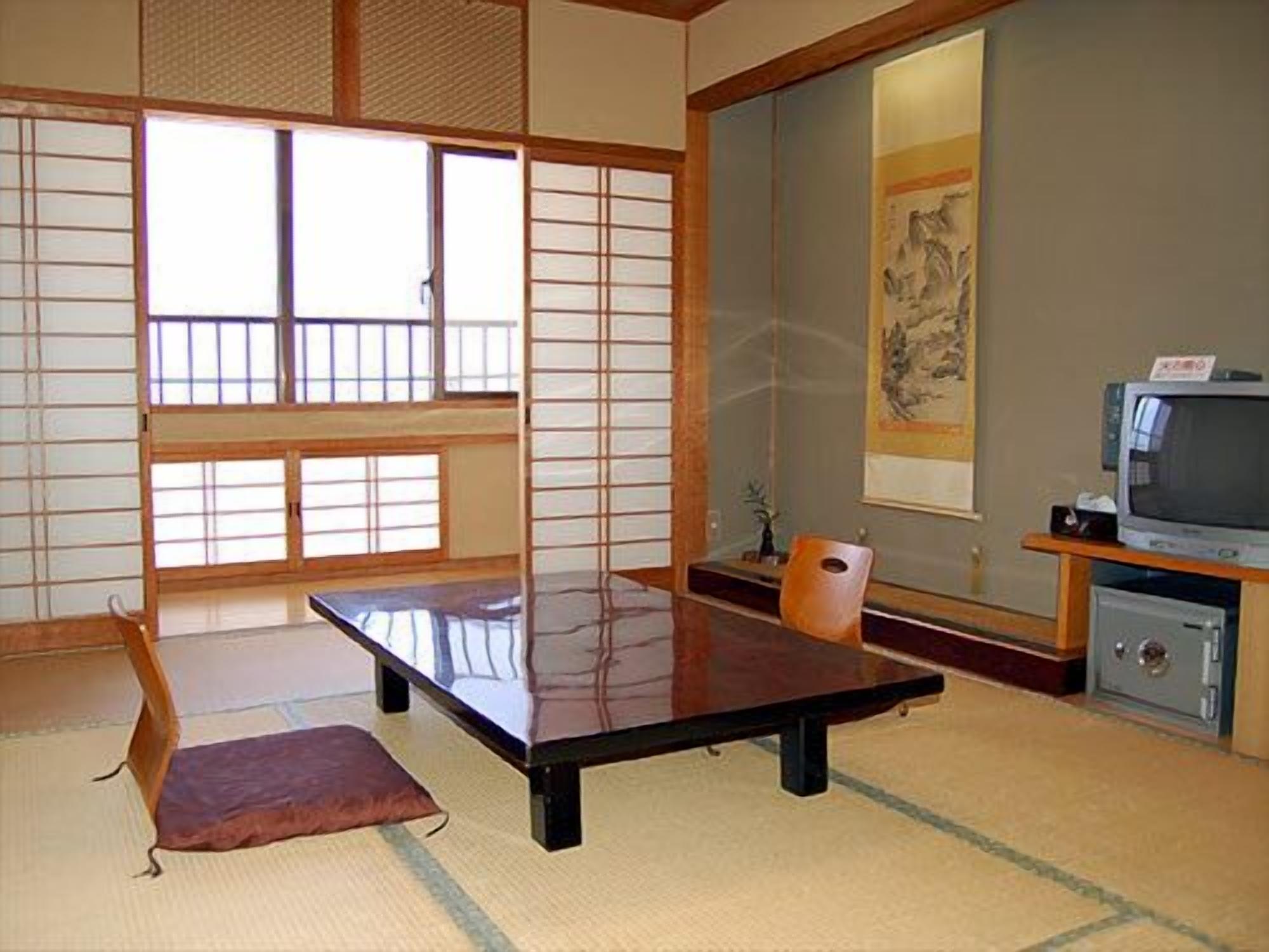 A traditional Japanese room with tatami flooring, a low table, a television, and a painting on the wall.