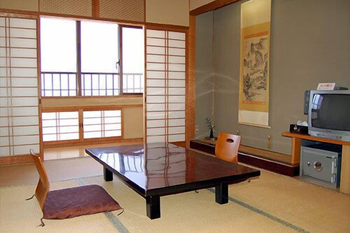 A traditional Japanese room with tatami flooring, a low table, a television, and a painting on the wall.