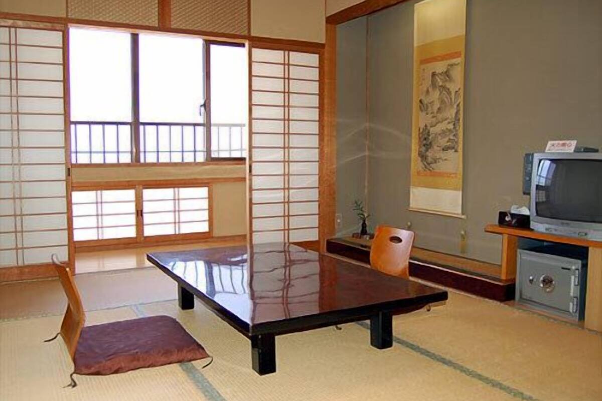 A traditional Japanese room with tatami flooring, a low table, a television, and a painting on the wall.