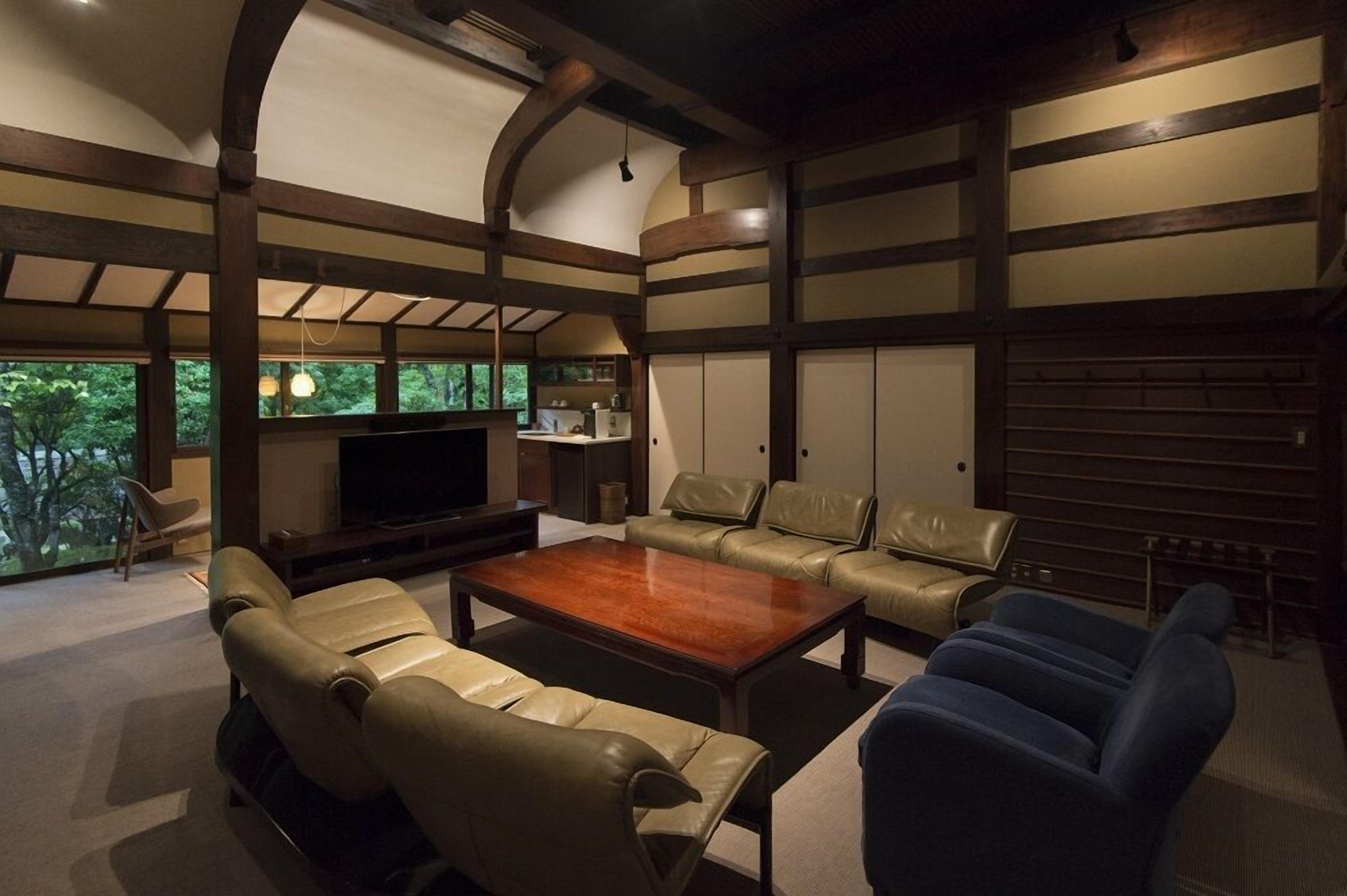 Un salón amplio con un televisor de pantalla plana grande, sofás de cuero, una mesa de centro de madera y vistas al verdor exterior.