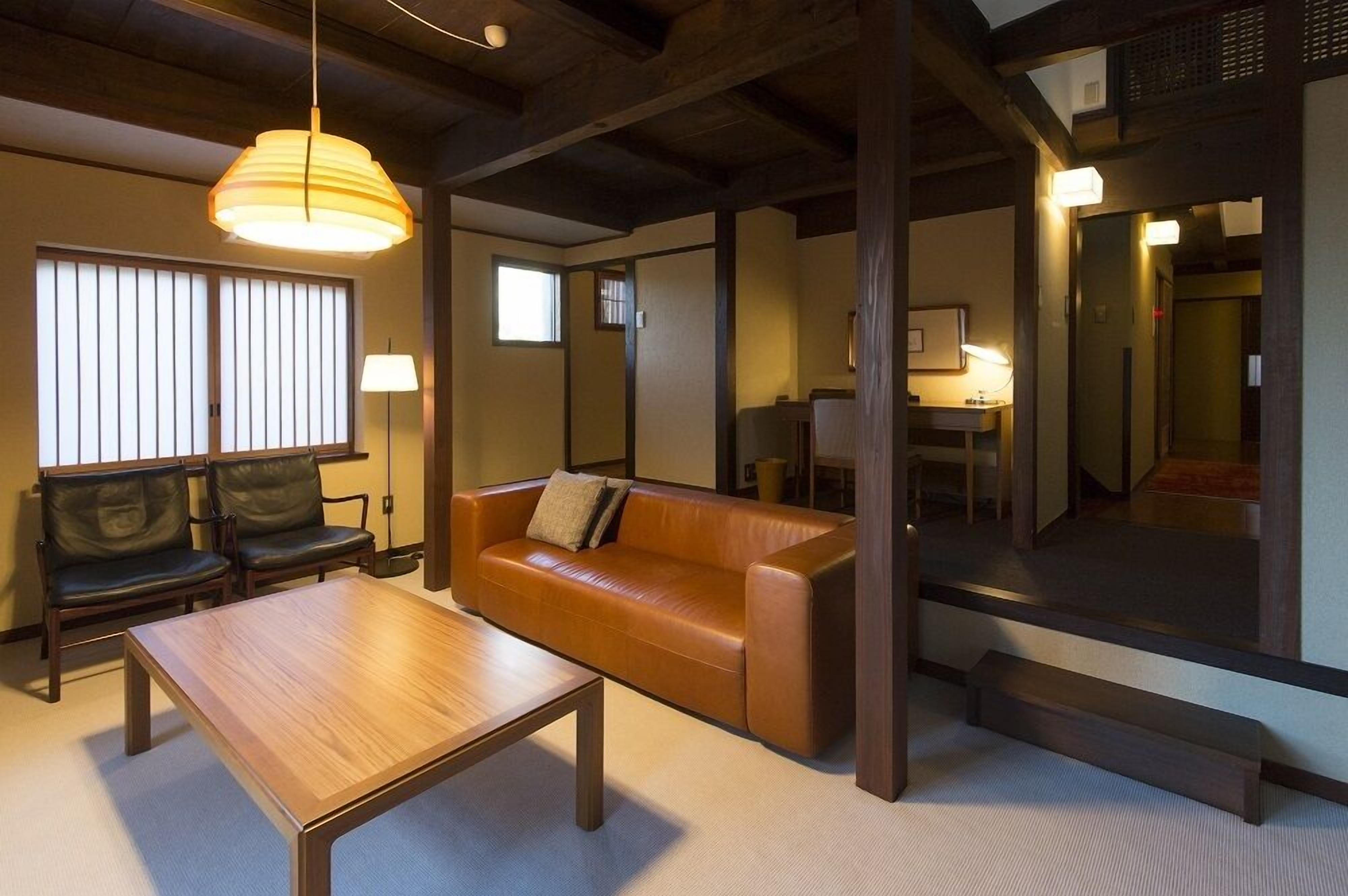 Una habitación de estilo japonés tradicional con suelo de tatami, una mesa de madera, un sofá de cuero y una lámpara colgante.