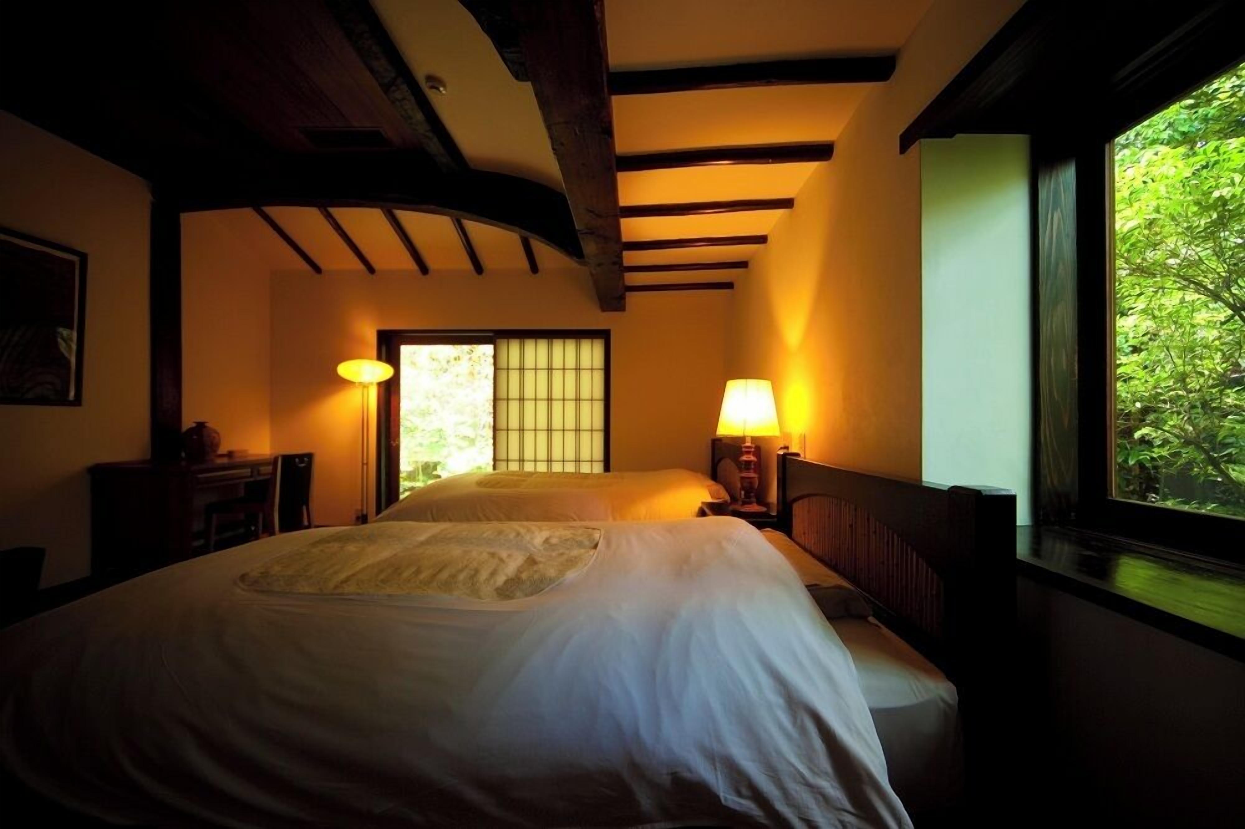 Una habitación con una cama grande, dos lámparas de noche, un ventanal con vistas a zonas verdes y un tradicional panel corredizo japonés.