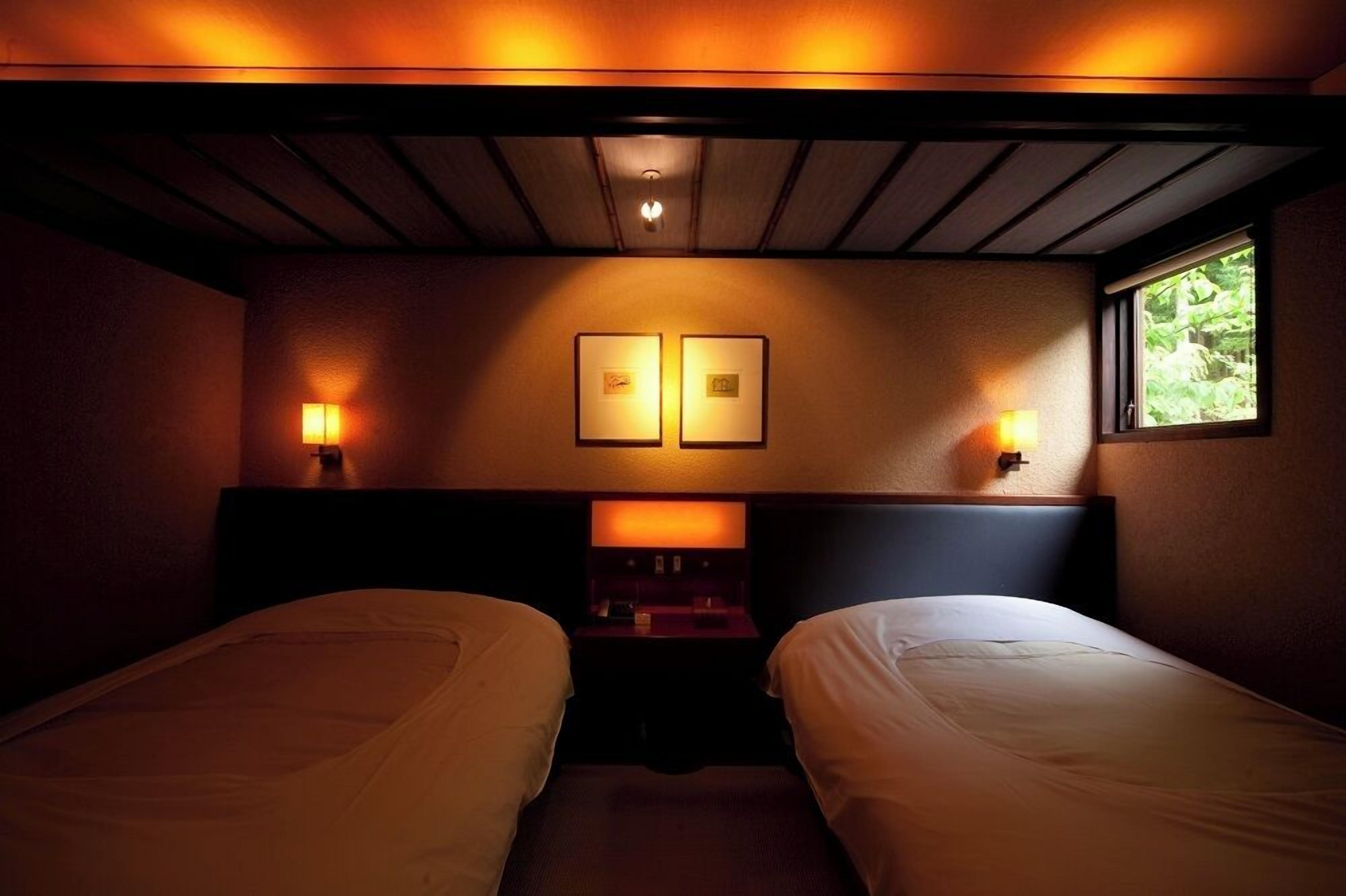 Una habitación con dos camas, cabeceras, lámparas de pared y una ventana con vistas.