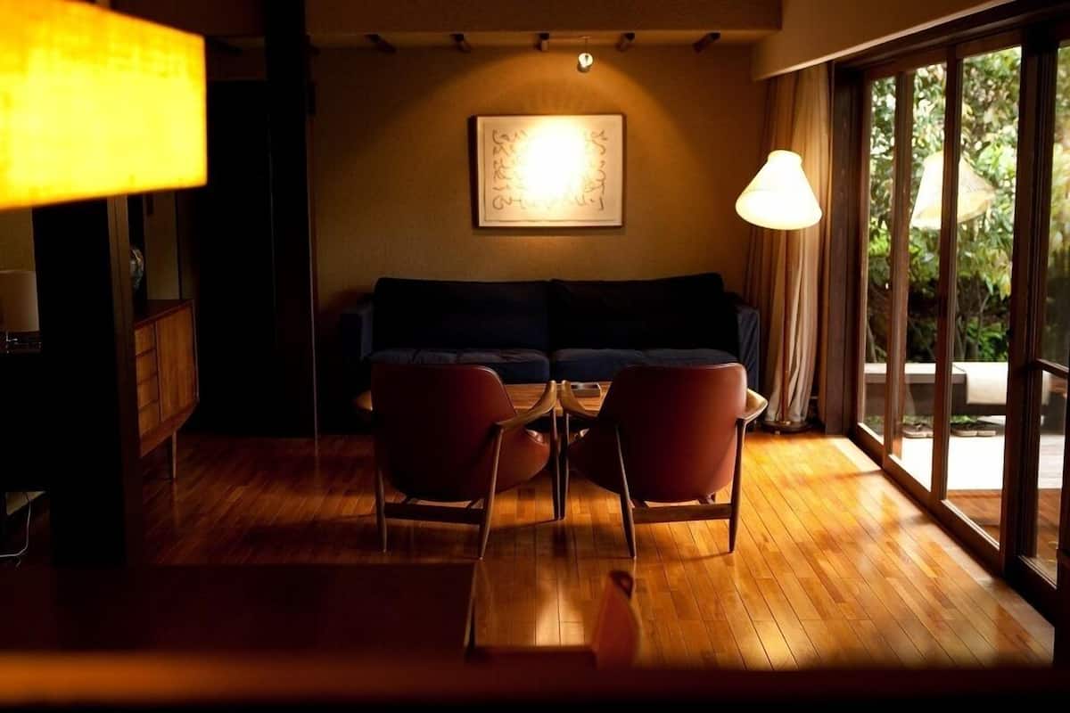 A room with a wooden floor, a sofa, two chairs, a table, and a window with a view of greenery.