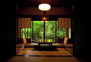 Ein traditioneller japanischer Raum mit Tatami-Boden, einem niedrigen Tisch und Schiebetüren, die zu einem Garten führen.