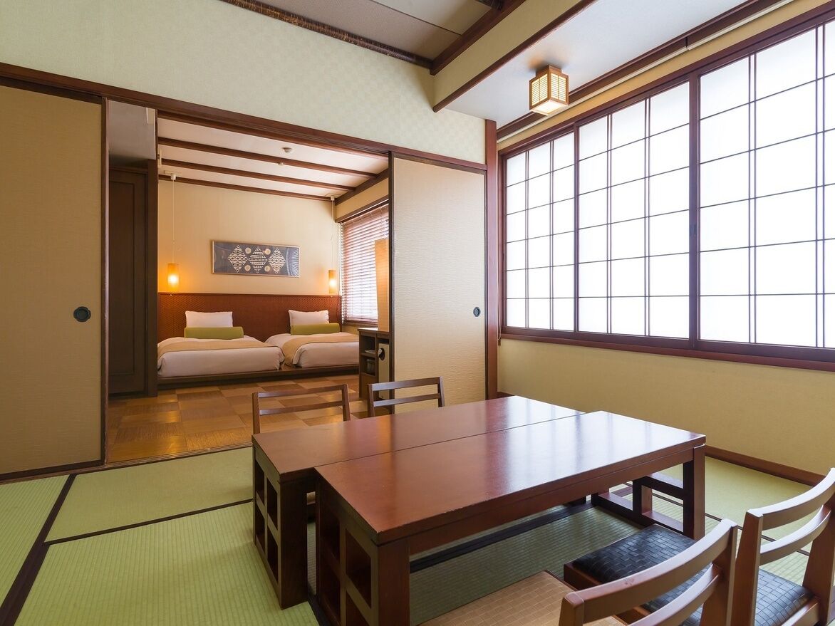 Une pièce de style japonais traditionnel, avec un sol recouvert de tatamis, une table en bois et un lit équipé d’un futon.