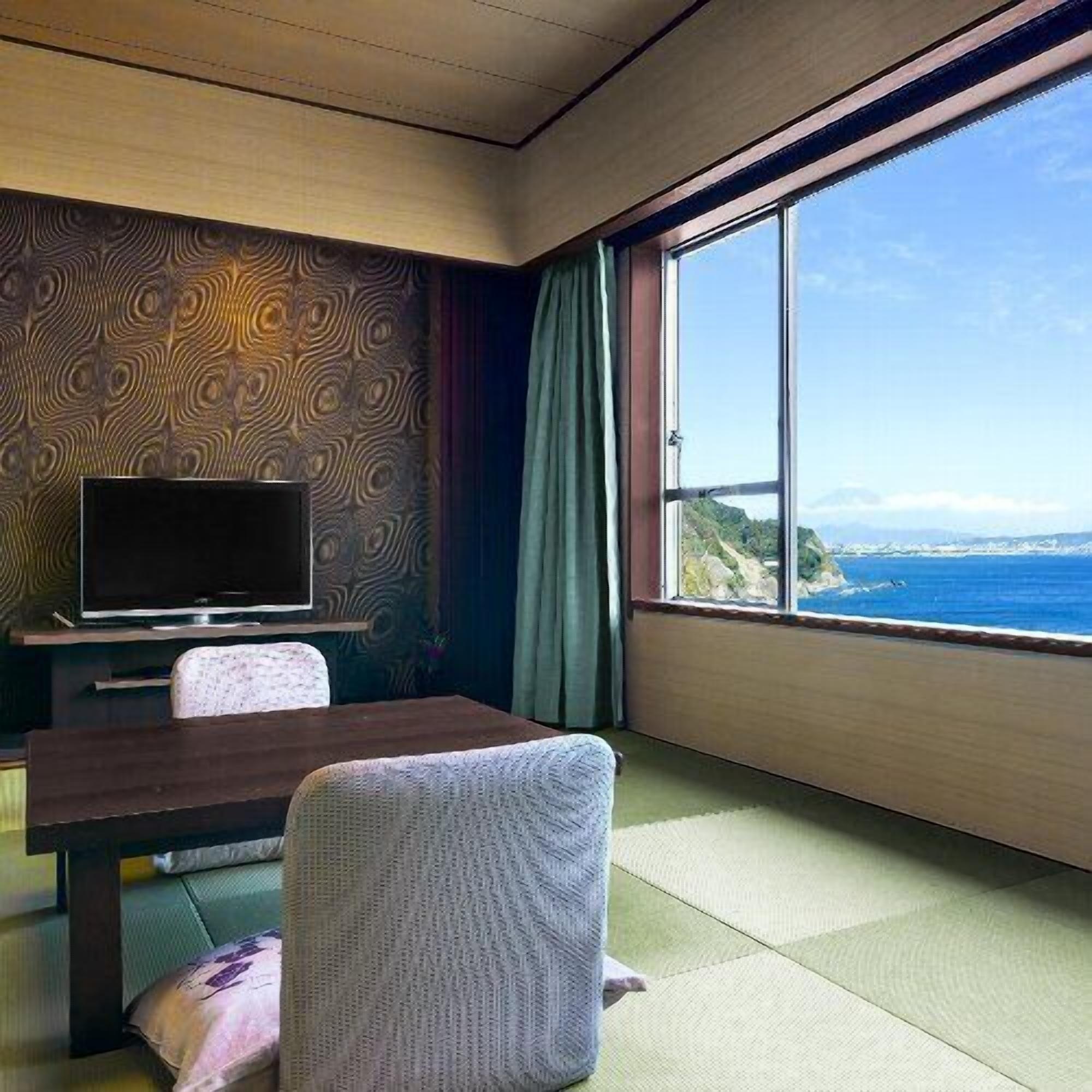 Una stanza con televisione, un tavolo, una sedia e un'ampia finestra vista mare.