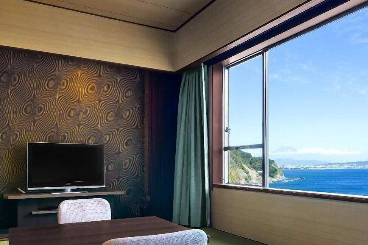 Ein Zimmer mit Fernseher, Tisch, Stuhl und einem großen Fenster mit Meerblick.