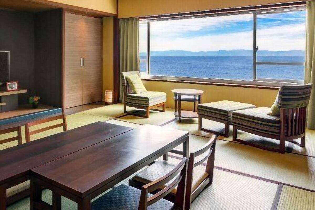 Ein Zimmer mit einem Holztisch, Stühlen, einem kleinen runden Tisch, einer Couch und einem großen Fenster mit Meerblick.