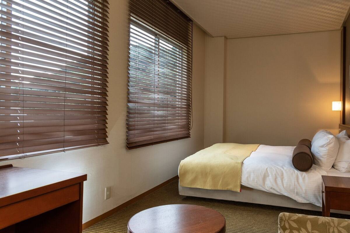 Una camera d'albergo con un letto, comodini, un tavolo rotondo e due finestre con tende.