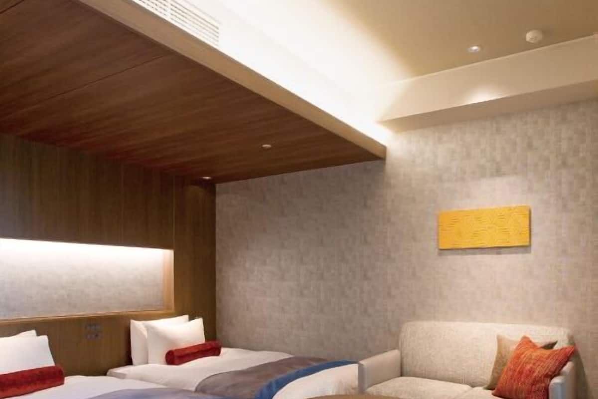 Ein Hotelzimmer mit zwei Betten, einem Sofa, einem kleinen Tisch und einem Bild an der Wand.